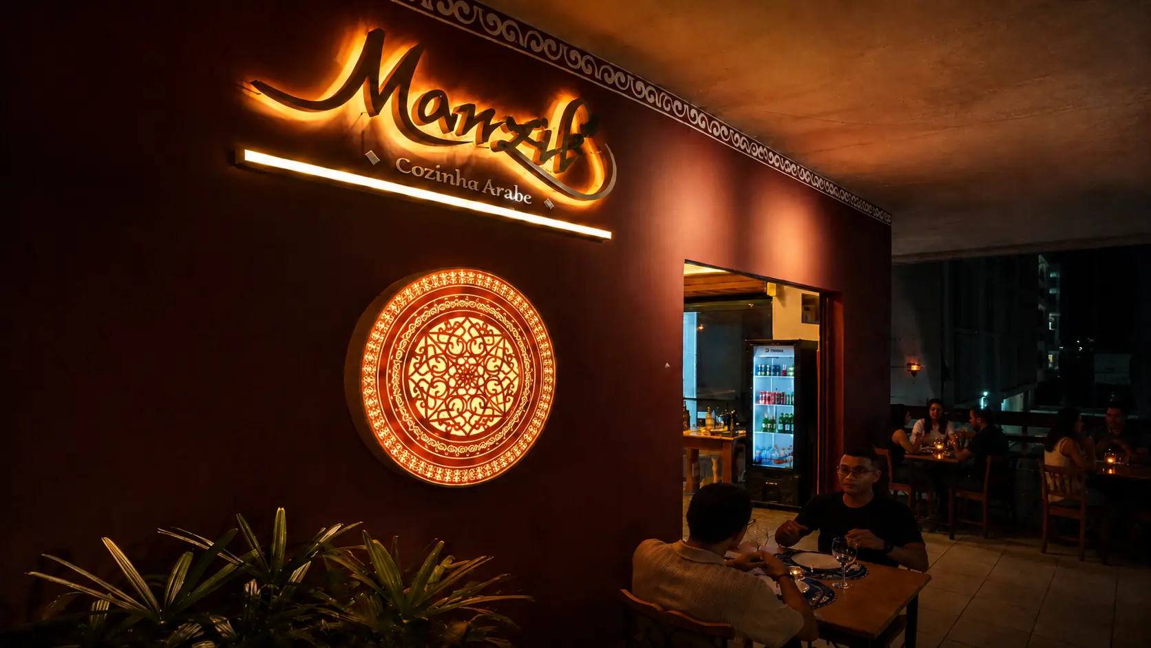 Fachada do restaurante árabe Manzil na Asa Norte, Brasília, com letreiro iluminado, mandala decorativa e mesas no salão